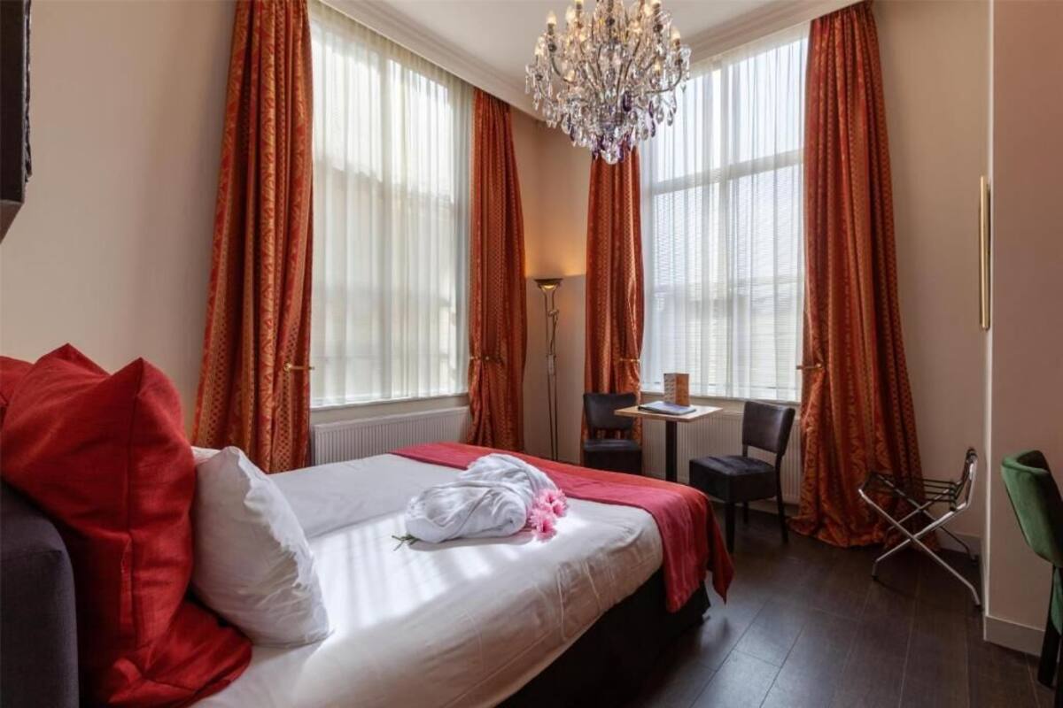 A hotel room with a bed, a desk, a chair, and a chandelier.