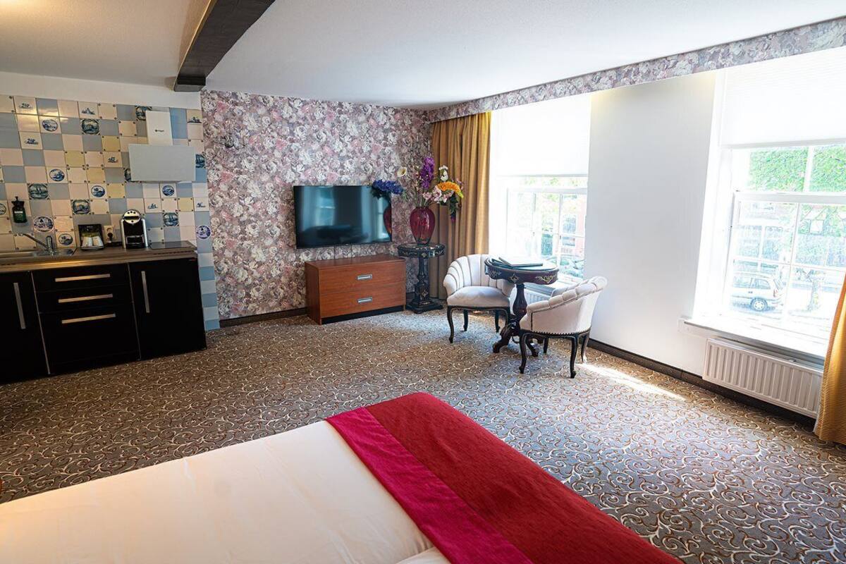 A hotel room with a bed, a desk, a chair, a TV, a dresser, and a window with curtains.