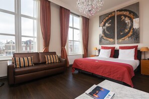 A hotel room with a large bed, a brown leather sofa, and a view of buildings outside the window. - Grand Museum Hotel, BW Signature Collection (Delft)