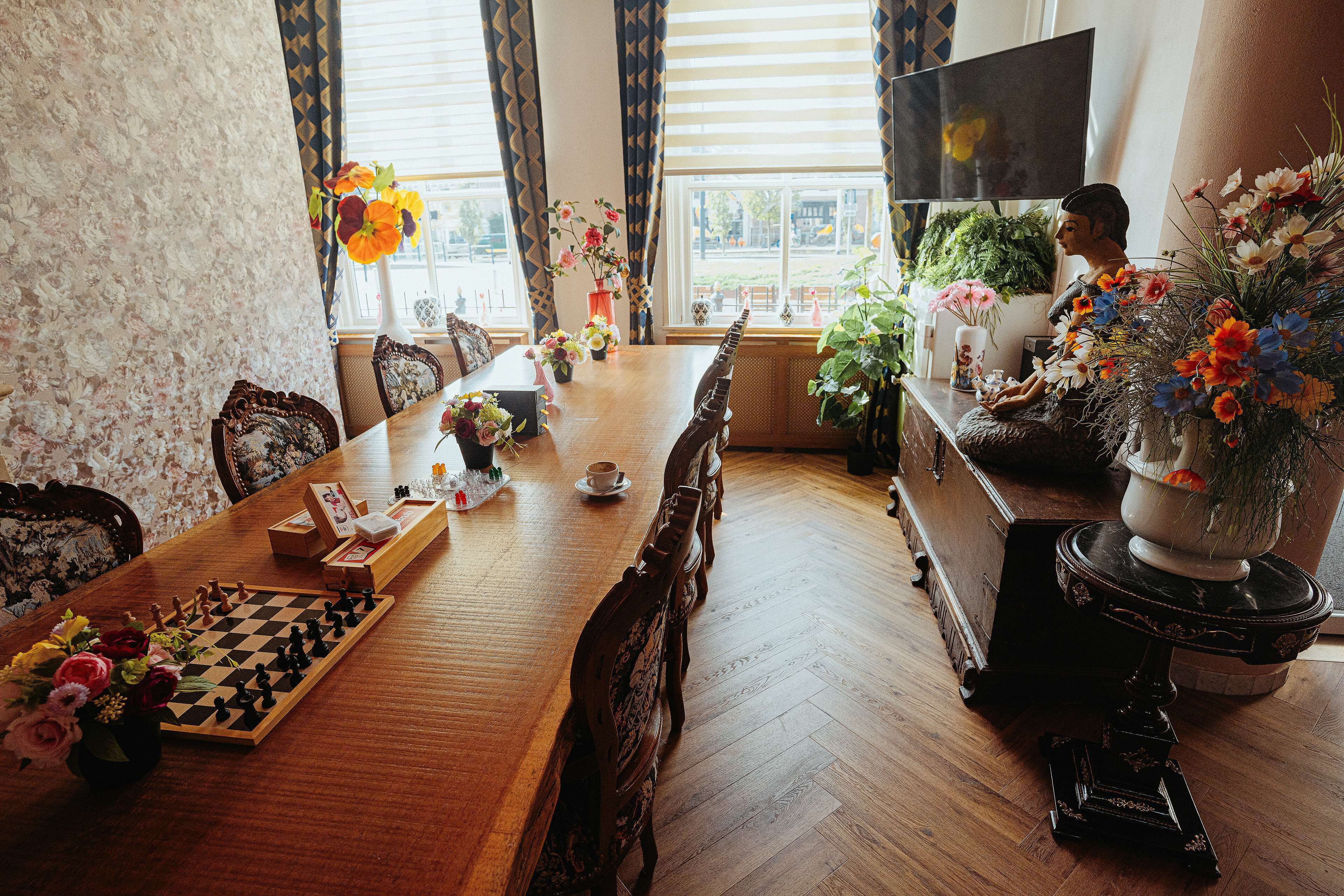 Un comedor con un tablero de ajedrez, arreglos florales y un televisor.