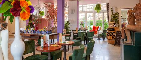 Un restaurante con sillas tapizadas de verde, un jarrón blanco con flores y una araña.