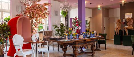 A lobby with a large table, chairs, a chandelier, and decorative plants.