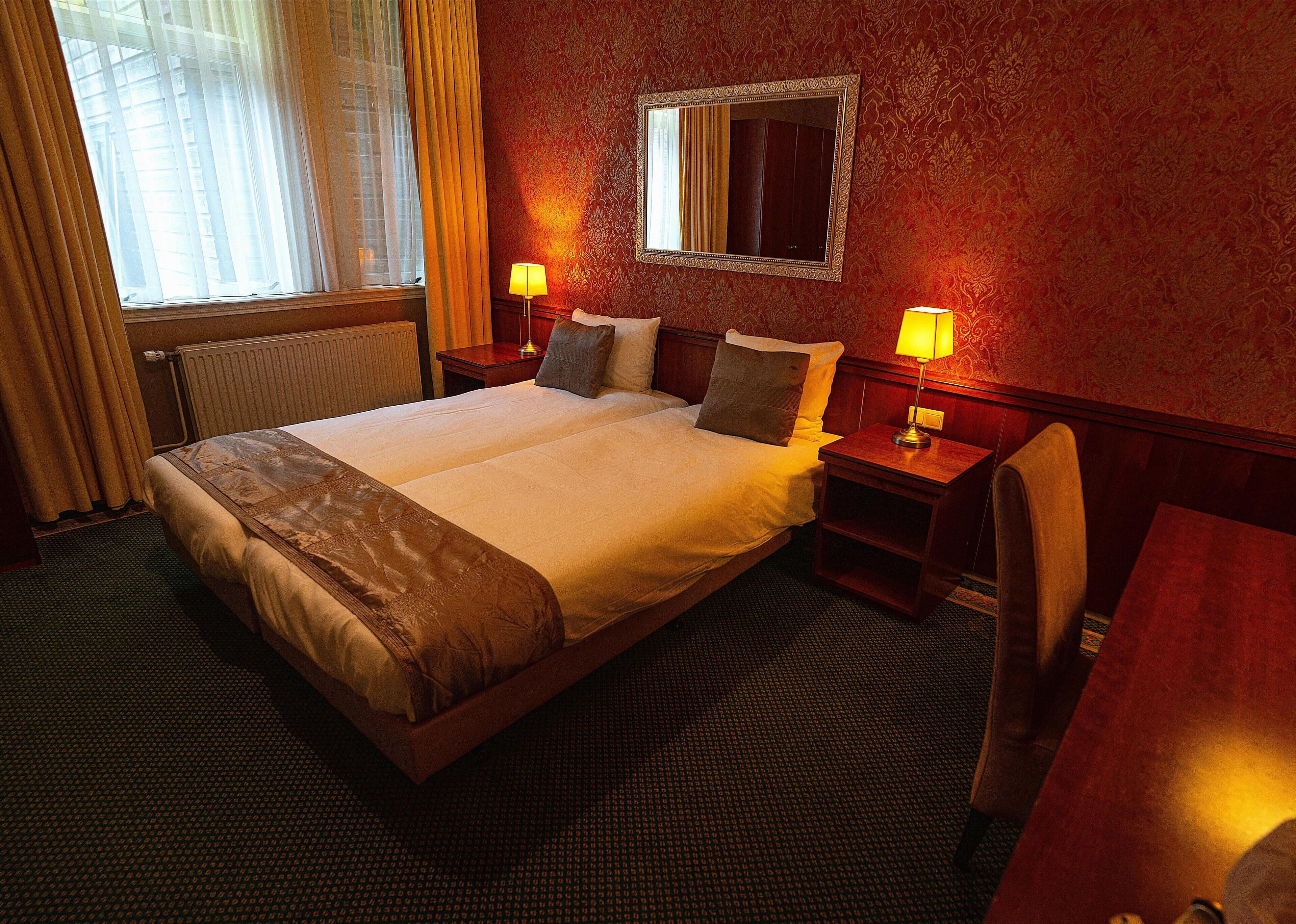 A hotel room with a large bed, two bedside tables with lamps, a mirror, and a window with curtains.