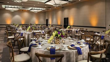 A banquet hall with round tables set for a formal event, featuring floral centerpieces and blue napkins.