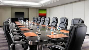 Un salón de conferencias con una mesa larga, sillas de cuero negro, botellas de agua y un televisor de pantalla plana en la pared.