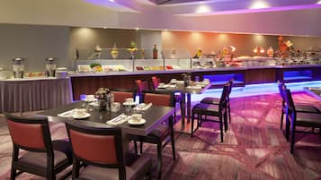 Un comedor de hotel con barra de desayuno buffet, varias mesas y sillas.
