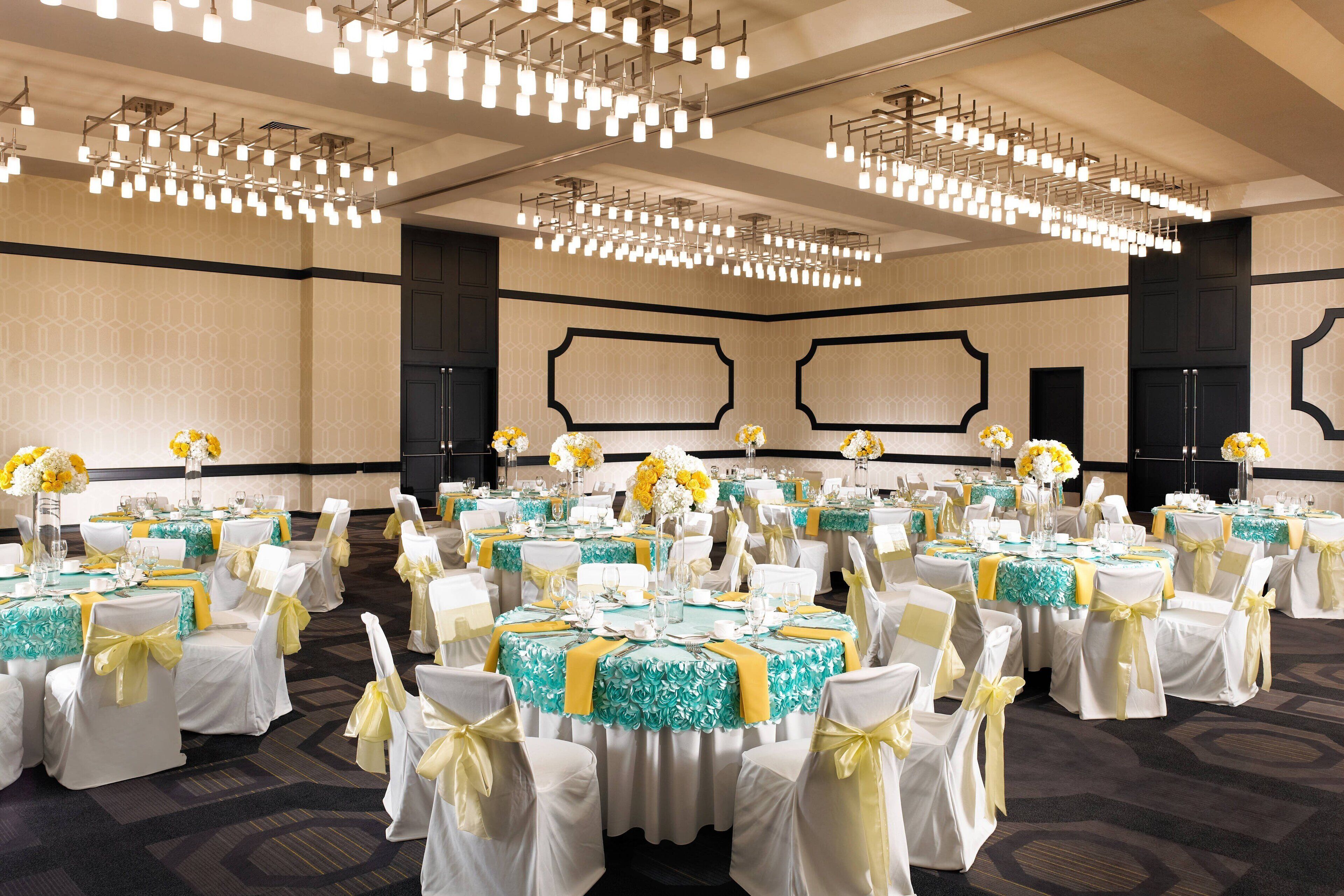 Une salle de banquet avec des tables rondes, des chaises blanches et des rubans jaunes.