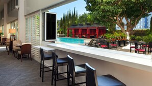 A poolside bar with seating, a pool, and a view of a red gazebo and trees.