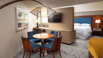 A hotel room with a dining area, a bed, a TV, and a desk.