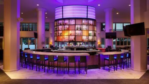 A bar area with a circular bar counter, multiple seating options, and a large illuminated shelf displaying various bottles.