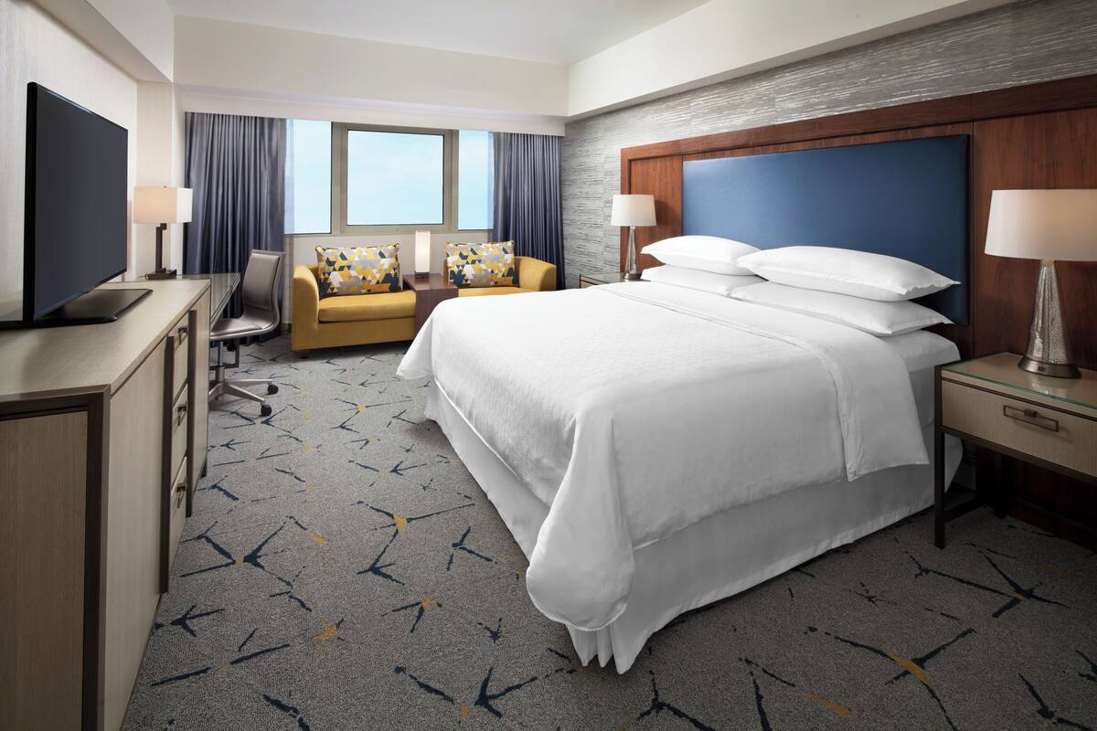 Une chambre d’hôtel avec un grand lit, un bureau avec une télévision, un canapé et une fenêtre avec des rideaux.