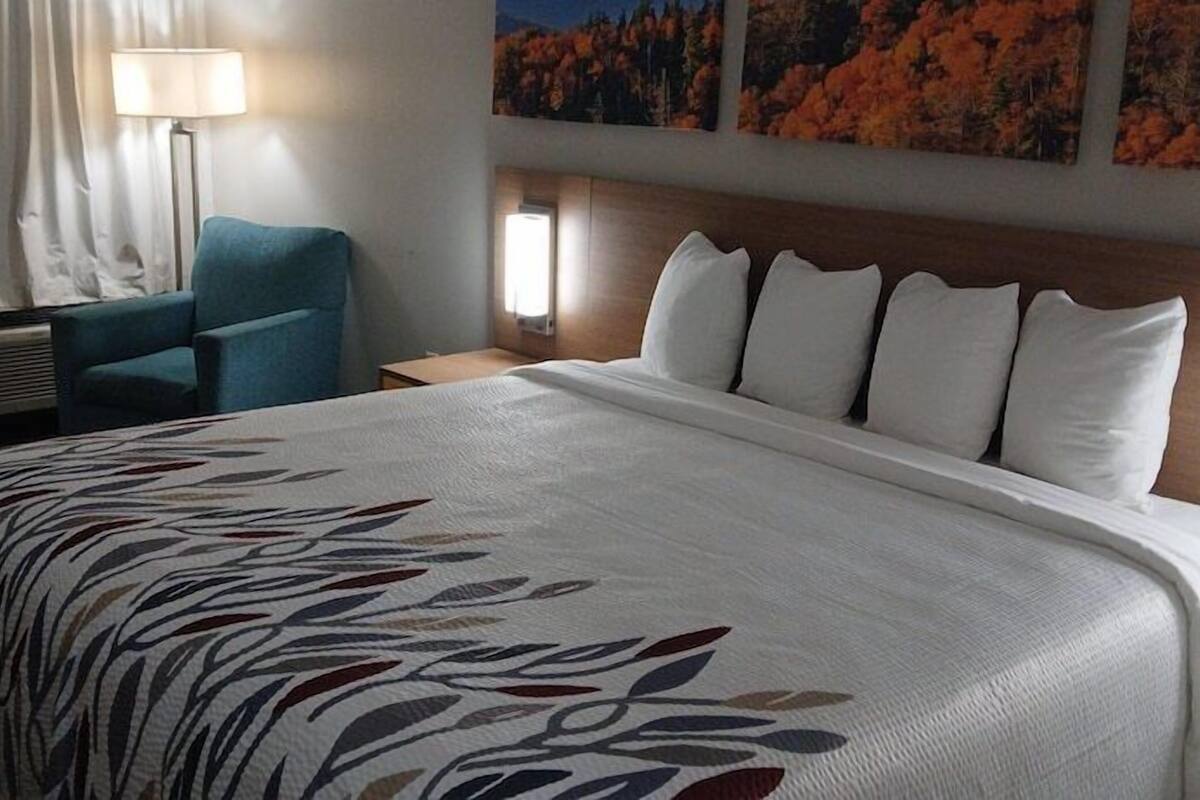 A hotel room with a large bed, a desk, a chair, and a wall-mounted lamp.