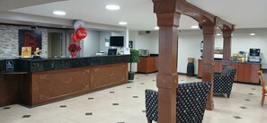 Uma área de recepção de hotel com balcão de mármore, placa da Red Roof e uma máquina de café.