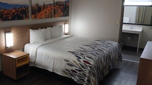 Et hotelværelse med seng, natbord og et badeværelse med vask og spejl.