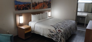 Een hotelkamer met een bed, nachtkastje en een badkamer met wastafel en spiegel.
