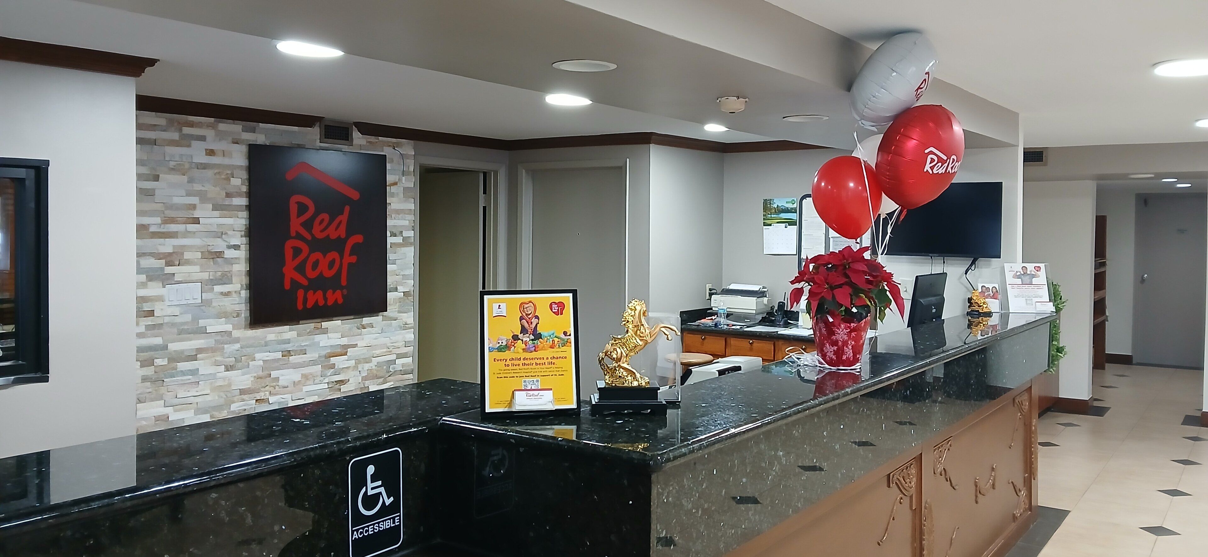 A reception area with a sign for Red Roof Inn, a reception desk, a wheelchair accessibility sign, and balloons.