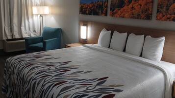 A hotel room with a large bed, a chair, a lamp, and a wall-mounted phone.