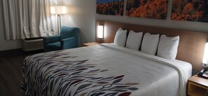 Quarto de hotel com uma cama grande, uma cadeira, um abajur e um telefone fixado na parede.