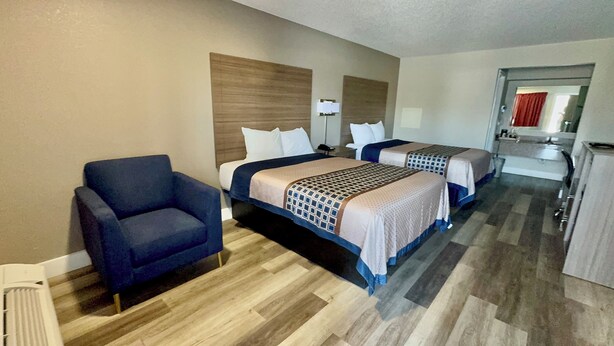 A hotel room with two beds, a blue armchair, a desk, and a mirror.