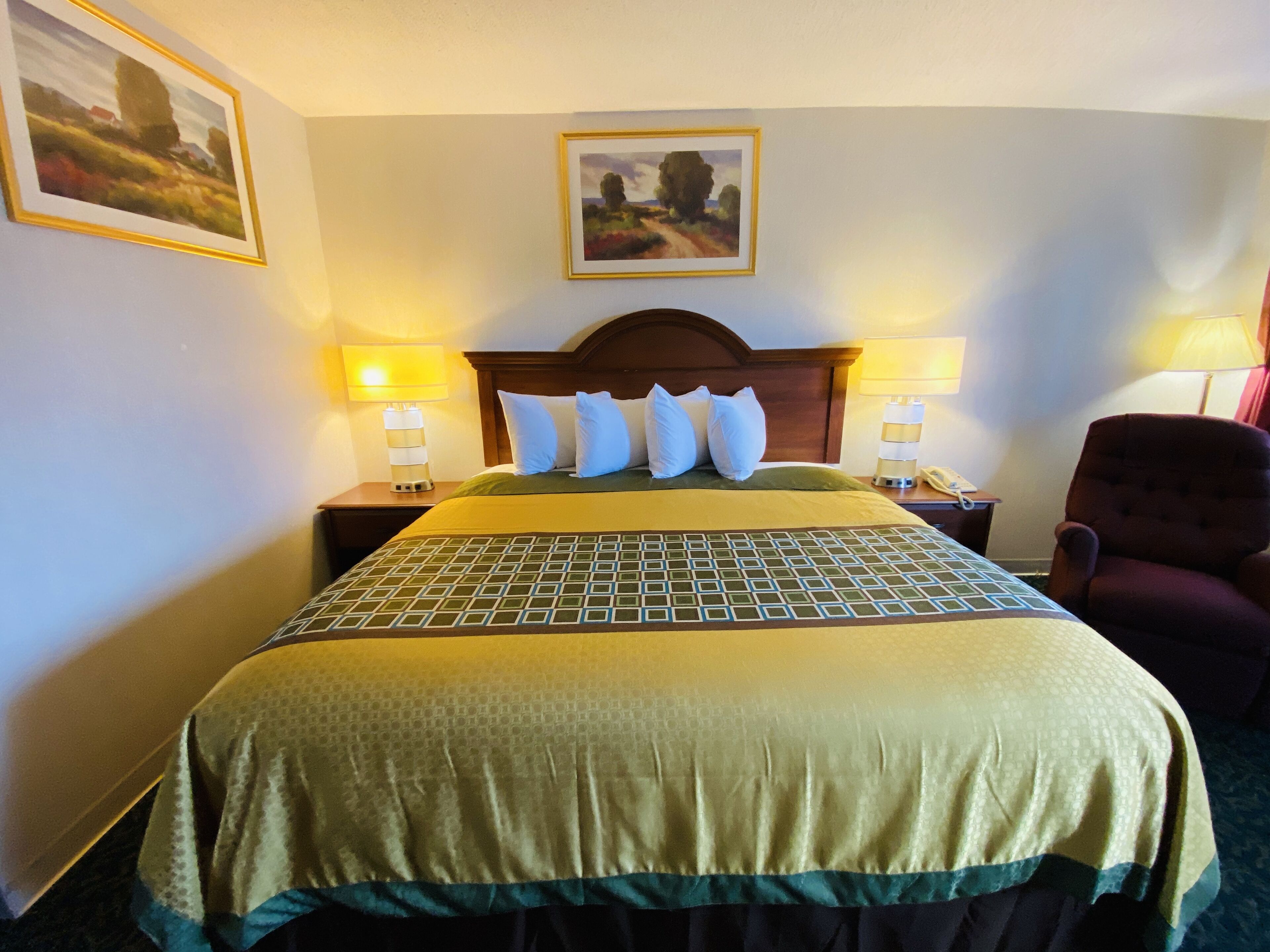 Una habitación de hotel con una cama grande, dos lámparas de noche, una silla y un cuadro enmarcado en la pared.