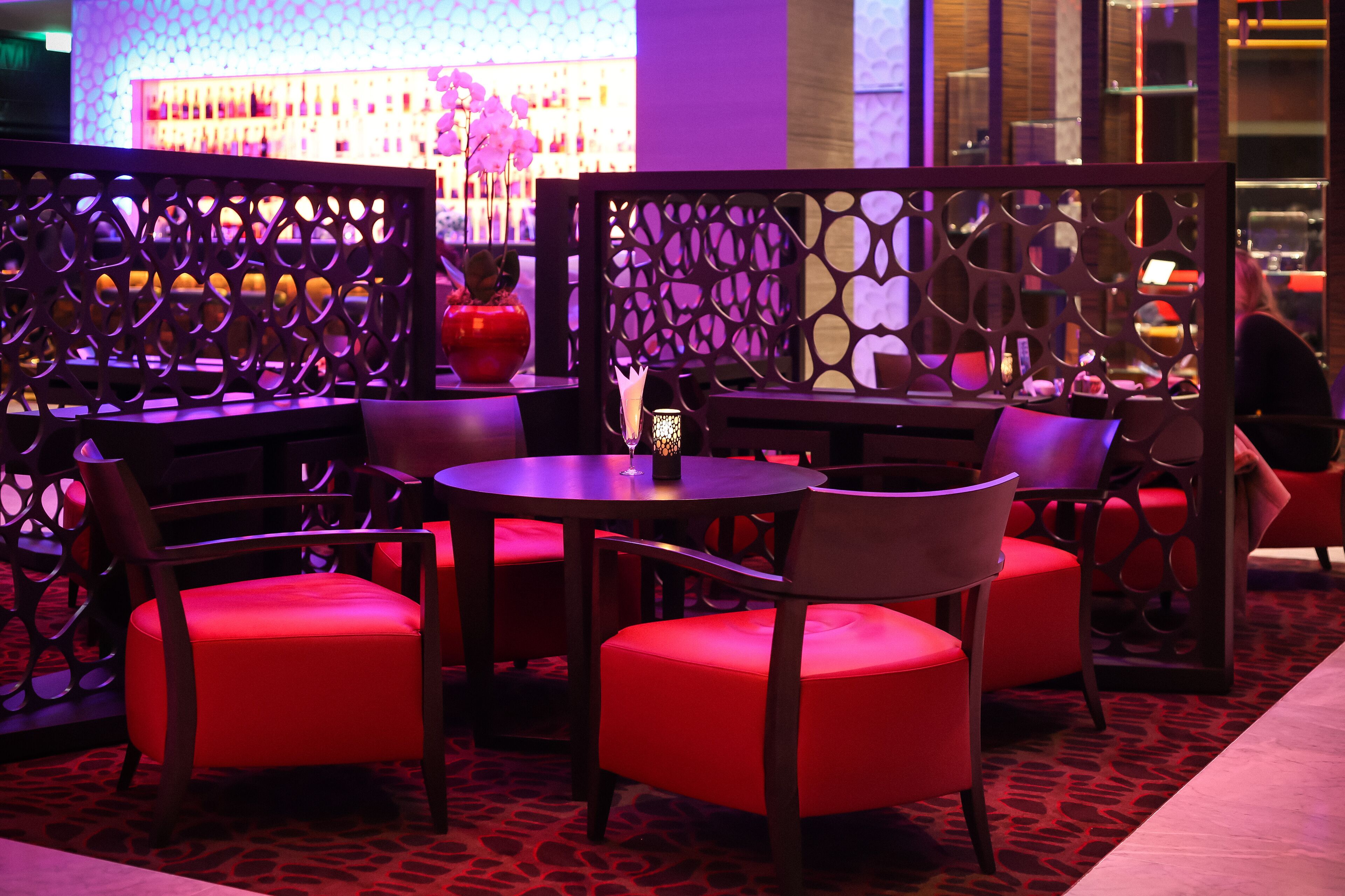 A section of a hotel with red upholstered chairs and tables, a decorative partition, and a patterned carpet.
