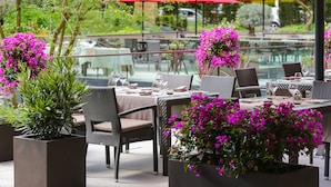 An outdoor dining area with tables set for two, surrounded by potted plants and red umbrellas.