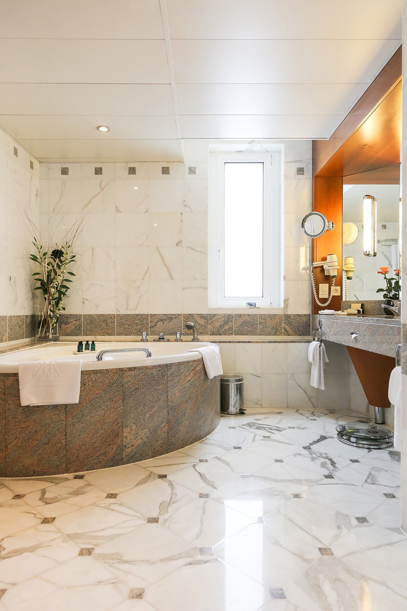 Une salle de bain moderne avec une baignoire sur pieds, un meuble-lavabo avec un miroir et une fenêtre laissant entrer la lumière naturelle.