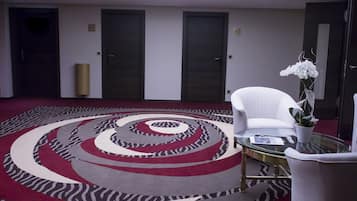 Een moderne hotellobby met een rond tapijt, een wit receptiebalie en een plafondlamp.