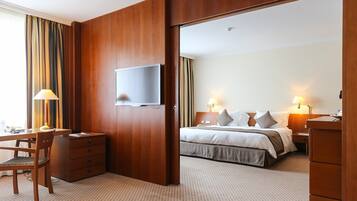 A hotel room with a bed, bedside tables, a desk with a chair, a television, and a wardrobe.