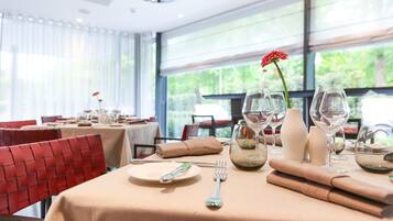 Una mesa de comedor dispuesta con platos, cubiertos y copas de vino, con un centro de mesa de flores rojas.