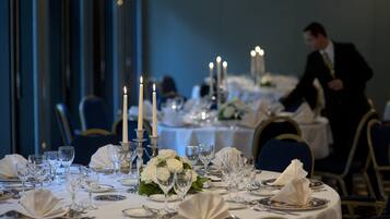 A formal dining room with tables set for a meal, candles, and a waiter in the background.