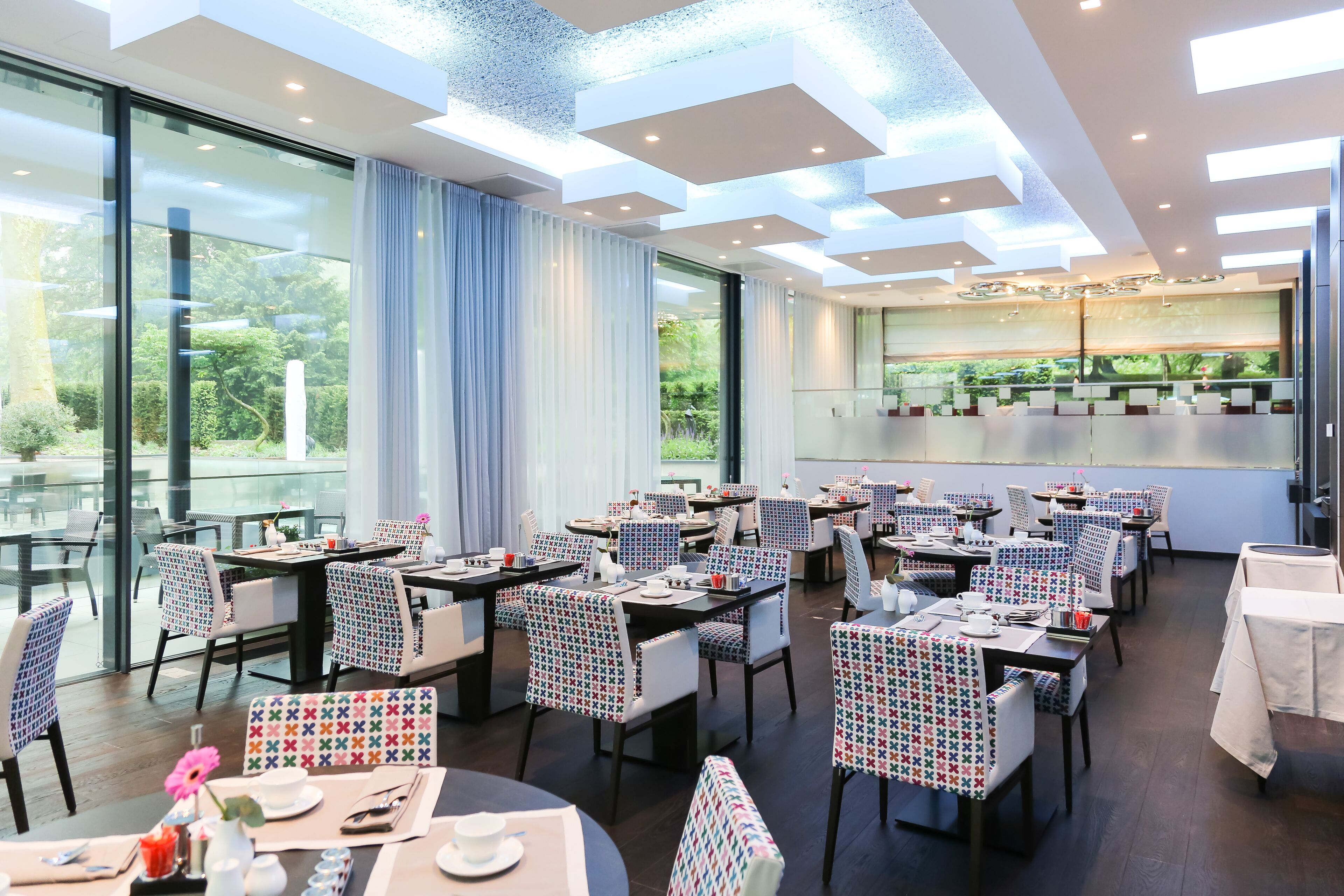 Un espace de restauration moderne avec des murs en verre, des tables et des chaises disposées avec soin, et une vue sur la verdure environnante.
