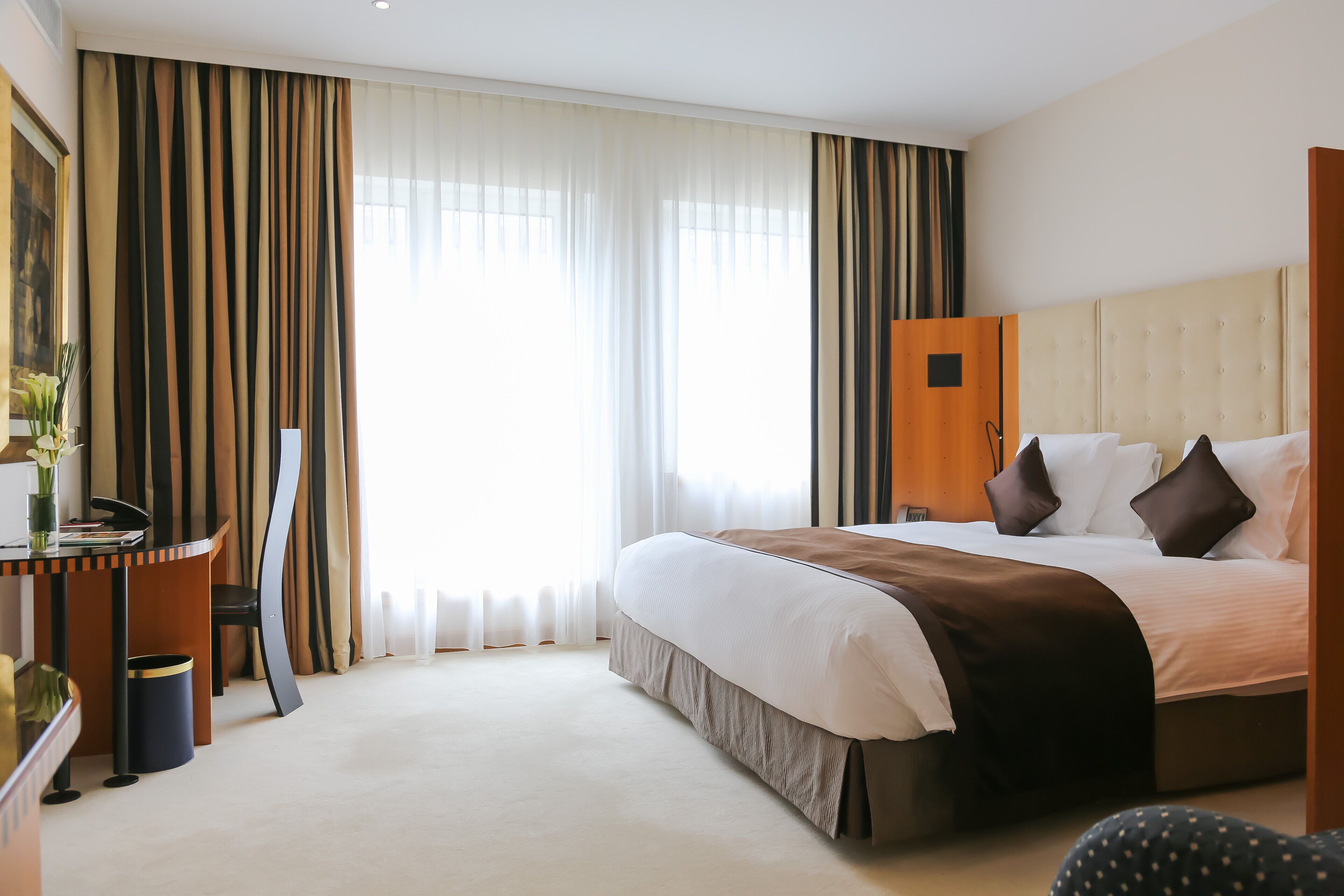 A hotel room with a large bed, a desk, and a wardrobe.