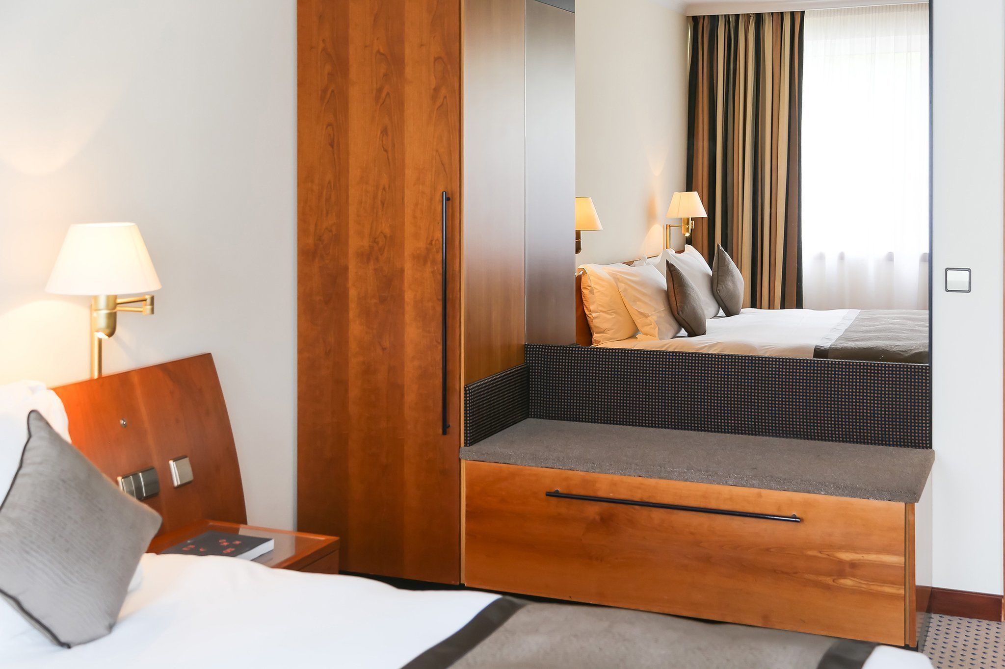 Une chambre d’hôtel comprenant un lit, une armoire en bois, un petit coin salon et une table de chevet avec une lampe.