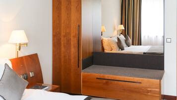 Une chambre d’hôtel comprenant un lit, une armoire en bois, un petit coin salon et une table de chevet avec une lampe.
