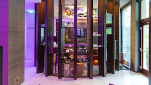 A modern hotel lobby with a central glass display case, wooden paneling, and a view of the outdoors.