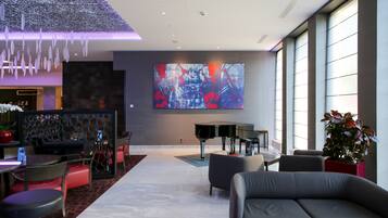 Un vestíbulo moderno con un piano de cola, asientos cómodos y un cuadro abstracto grande en la pared.
