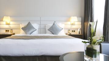 A hotel room with a large bed, two bedside tables with lamps, and a vase with flowers on a round table.