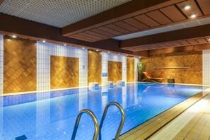An indoor swimming pool with tiled walls and a blue floor, surrounded by seating and a patterned wall. - Le Royal Hotels & Resorts (Luxembourg City)