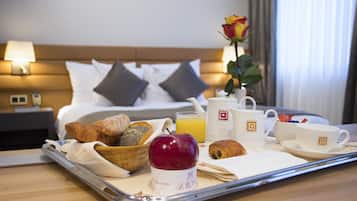 Een ontbijtkar met croissants, een appel en een koffiekop op een tafel in een hotelkamer.