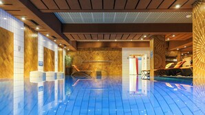 A spacious indoor swimming pool with a blue floor, surrounded by walls with a geometric pattern and a ceiling with recessed lighting.