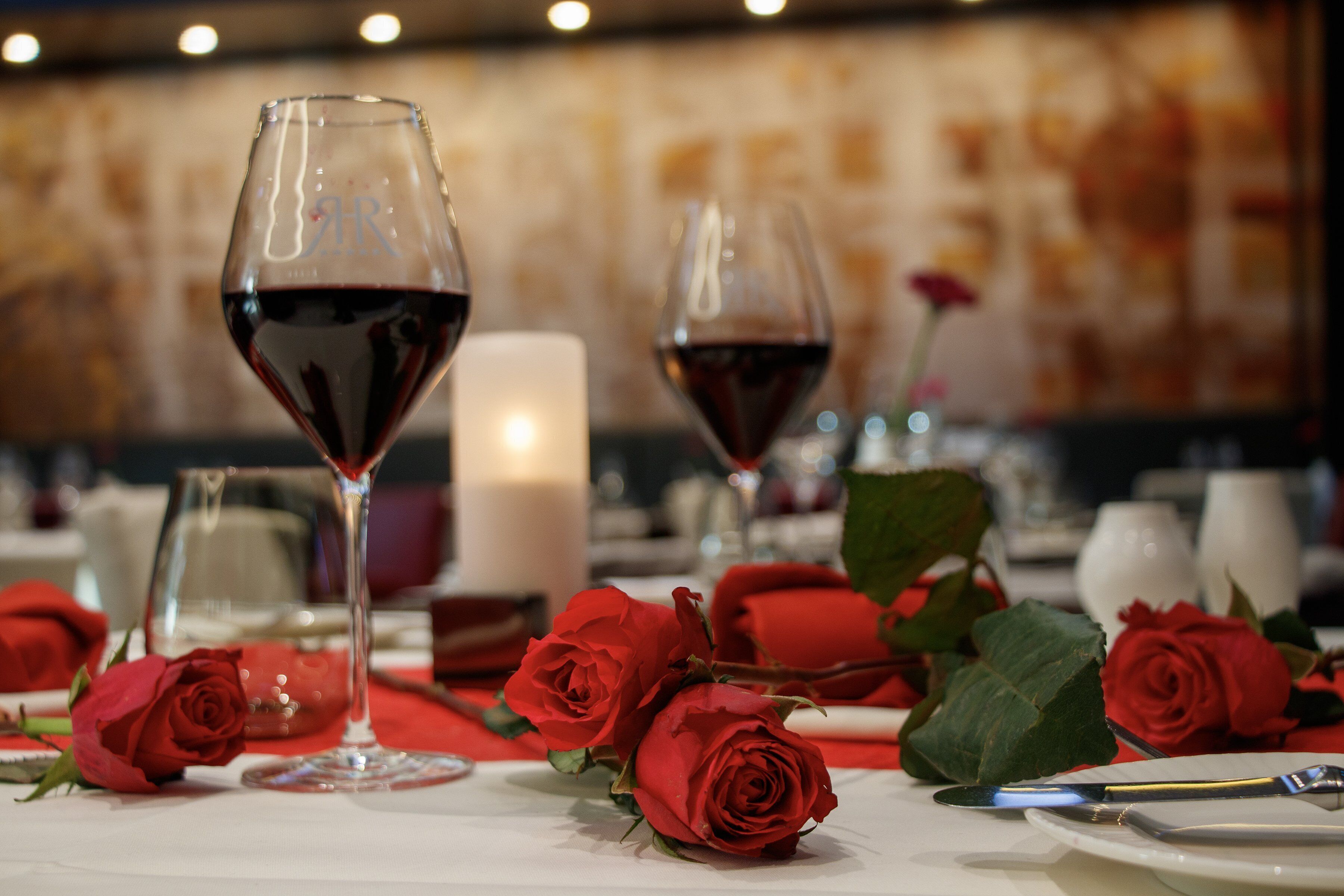 Una mesa dispuesta con copas de vino, rosas rojas y una vela, evocando un ambiente romántico para cenar.