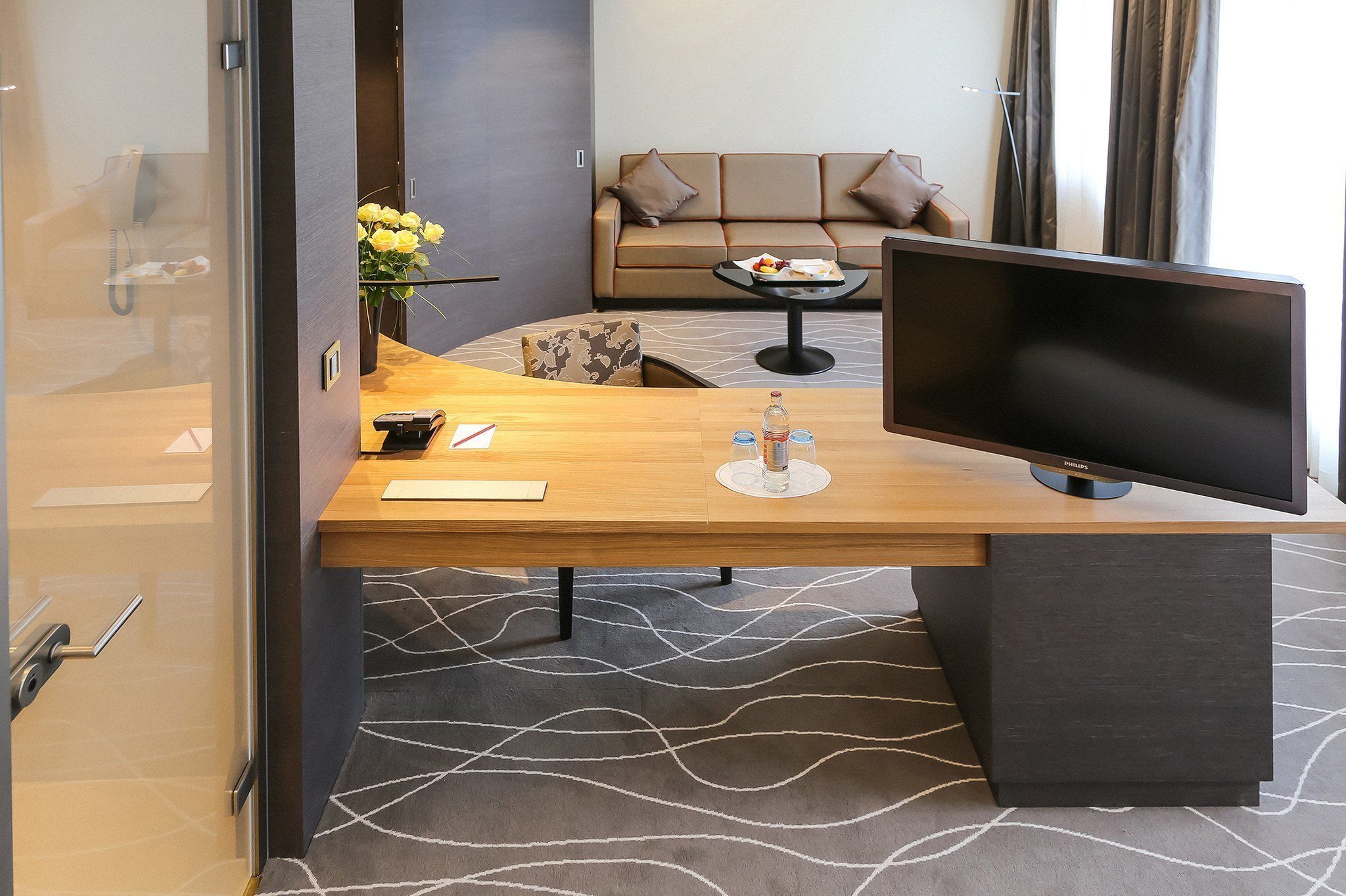 A hotel room with a wooden desk, a flat-screen TV, a sofa, and a coffee table.