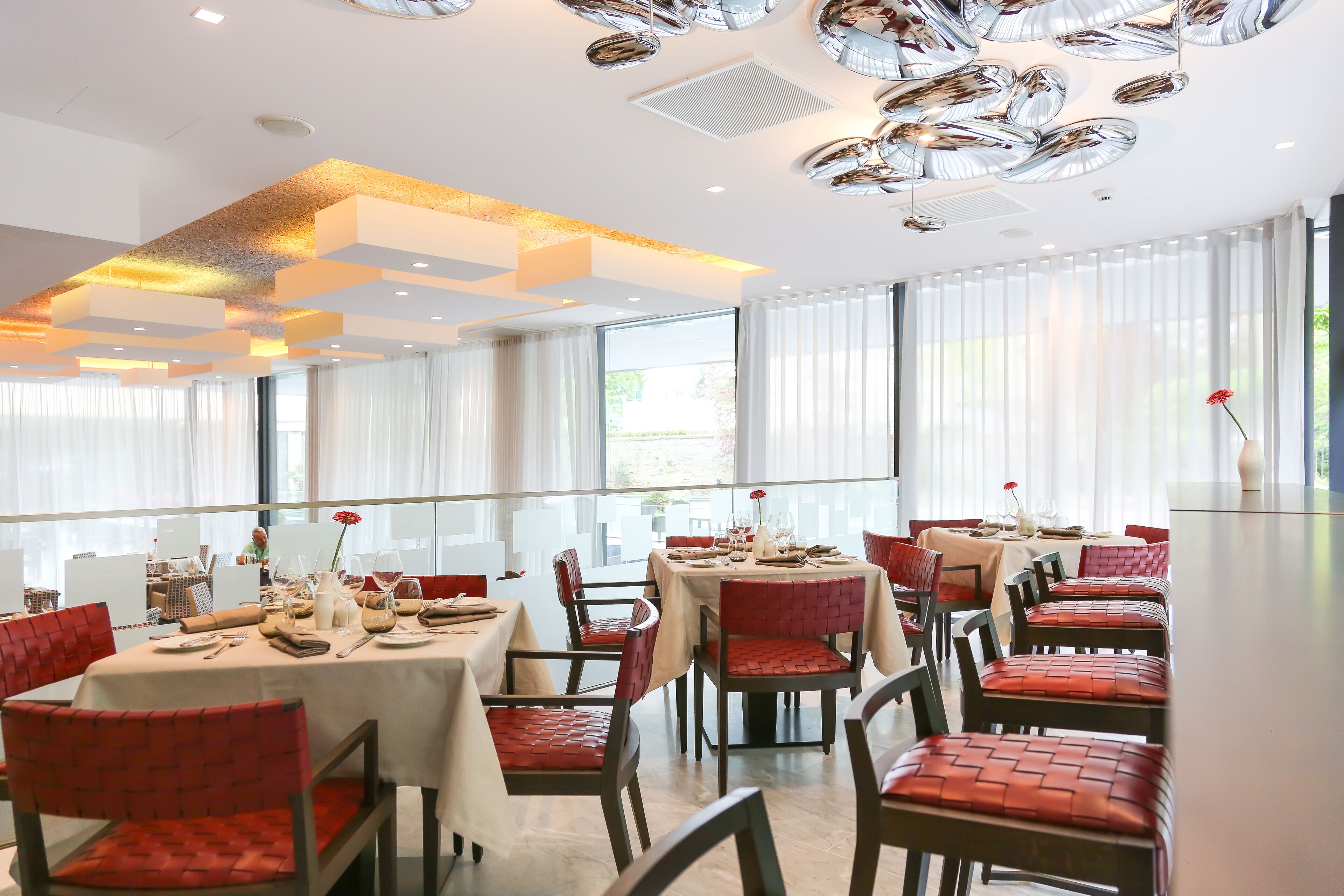 A dining area with tables set for service, red upholstered chairs, and a modern ceiling design.