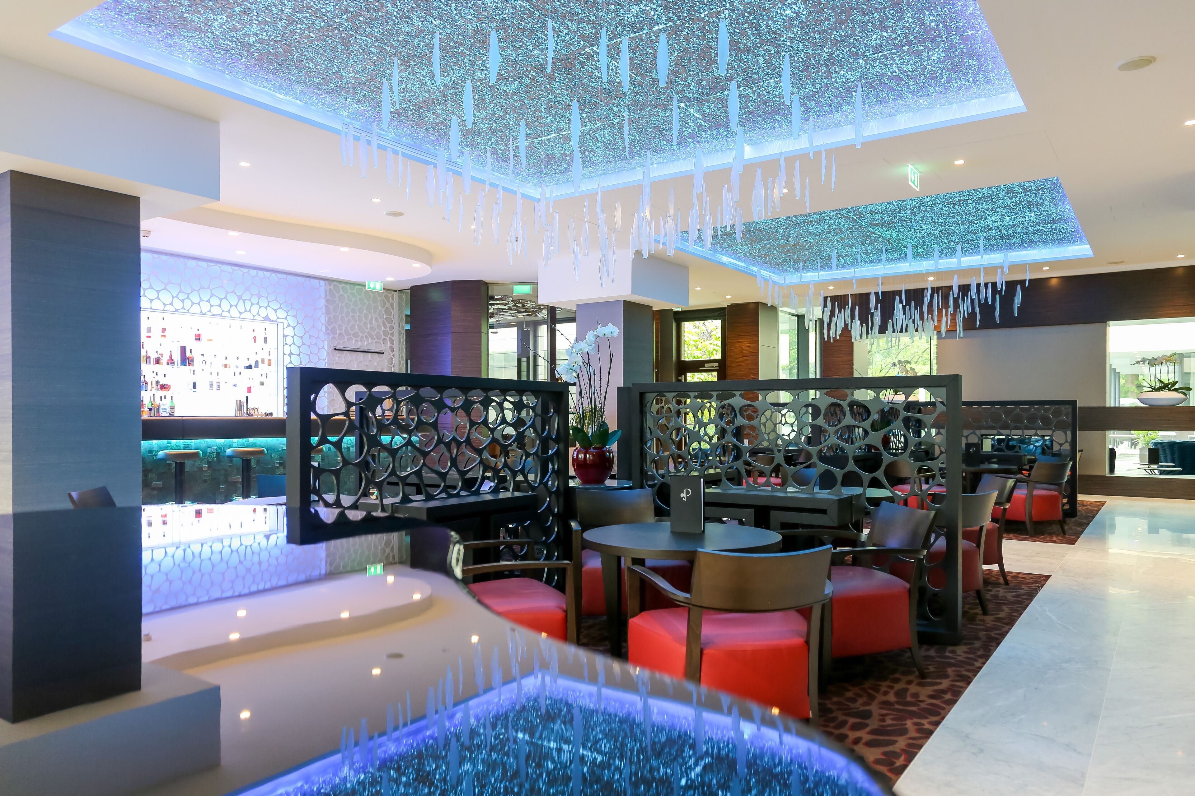 A modern hotel lobby with a bar area, seating arrangements, and decorative lighting.