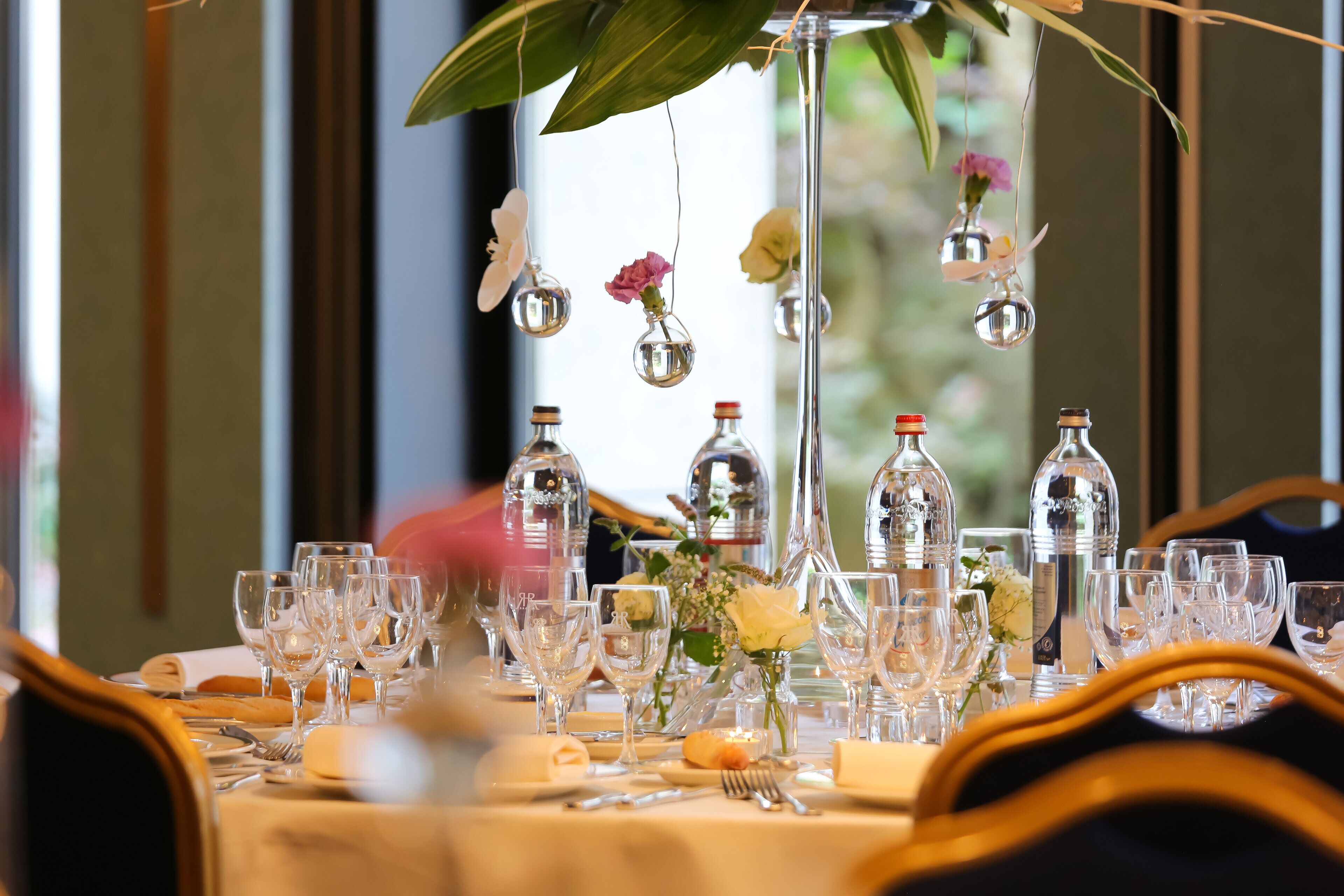 Ein Tisch, festlich für ein formelles Dinner gedeckt, mit mehreren Weingläsern, einer Blumendekoration und hängenden Glasornamenten.
