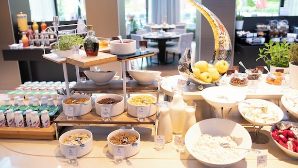 A buffet with various food and drink options, including bowls of cereal, fruits, and bottles of milk.