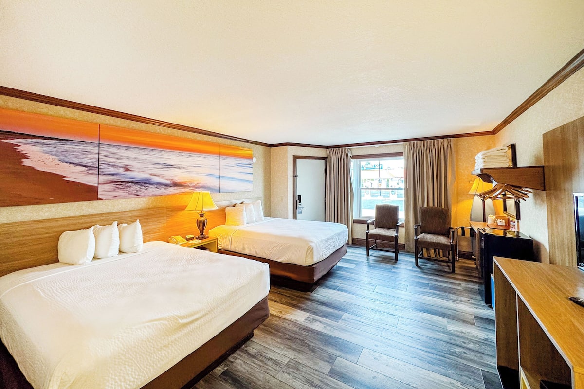 Ein Hotelzimmer mit zwei Betten, einem Schreibtisch, einem Sessel und einem großen Gemälde an der Wand.
