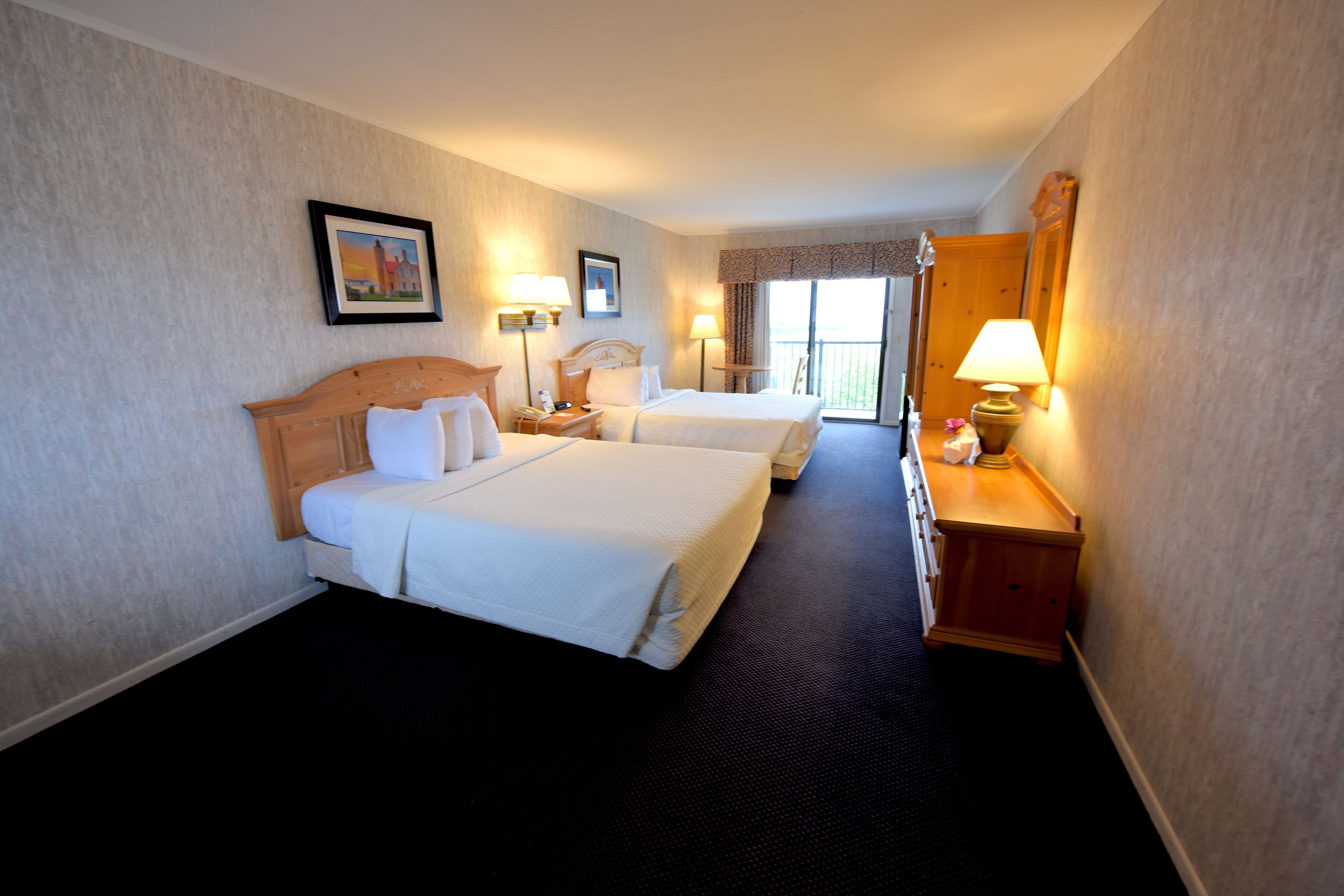 Habitación de hotel con dos camas, una mesita de noche, una lámpara y un cuadro en la pared.
