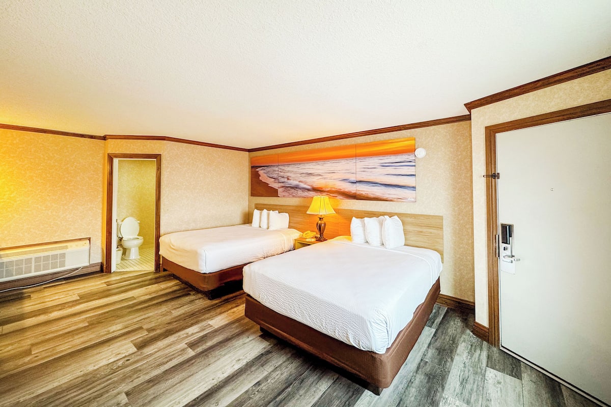 Ein Hotelzimmer mit zwei Betten, einem Sonnenuntergangsbild, einem Heizkörper und einer Tür.
